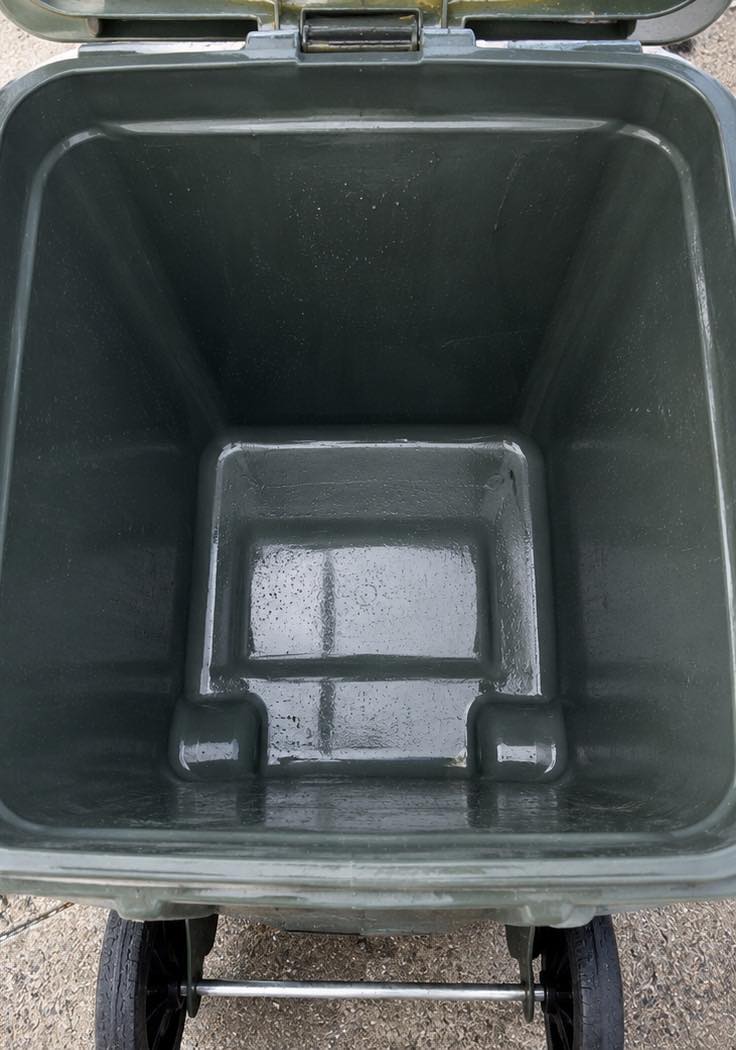 Looking down into a wheelie bin after cleaning: the interior is bare dark-green plastic with no residue left, still wet from the rinse.